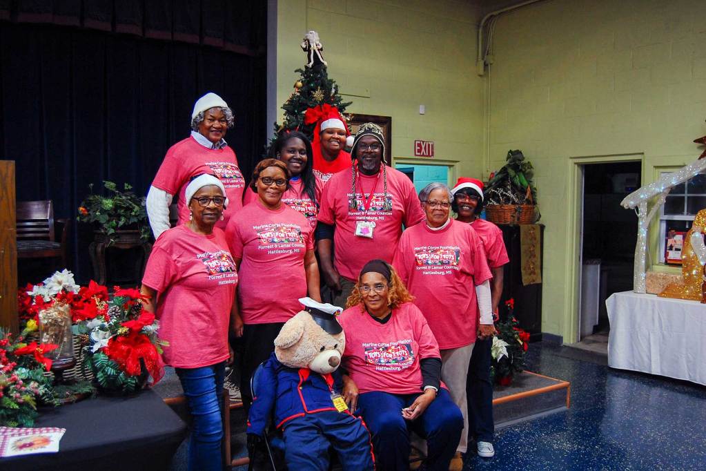 A group of people in matching red tshirts stand together in front of a small auditorium stage decorated for Christmas