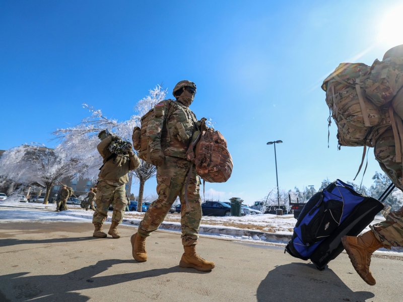 national guard members walk down a driveway amid ice-frozen trees