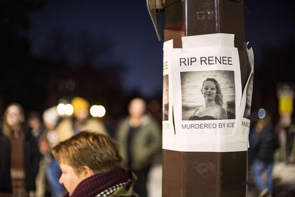A flyer on a lightpole reads "RIP Renee - Murdered by Ice" with a photo of a woman shown. A large crowd is visible beyond the lightpole.