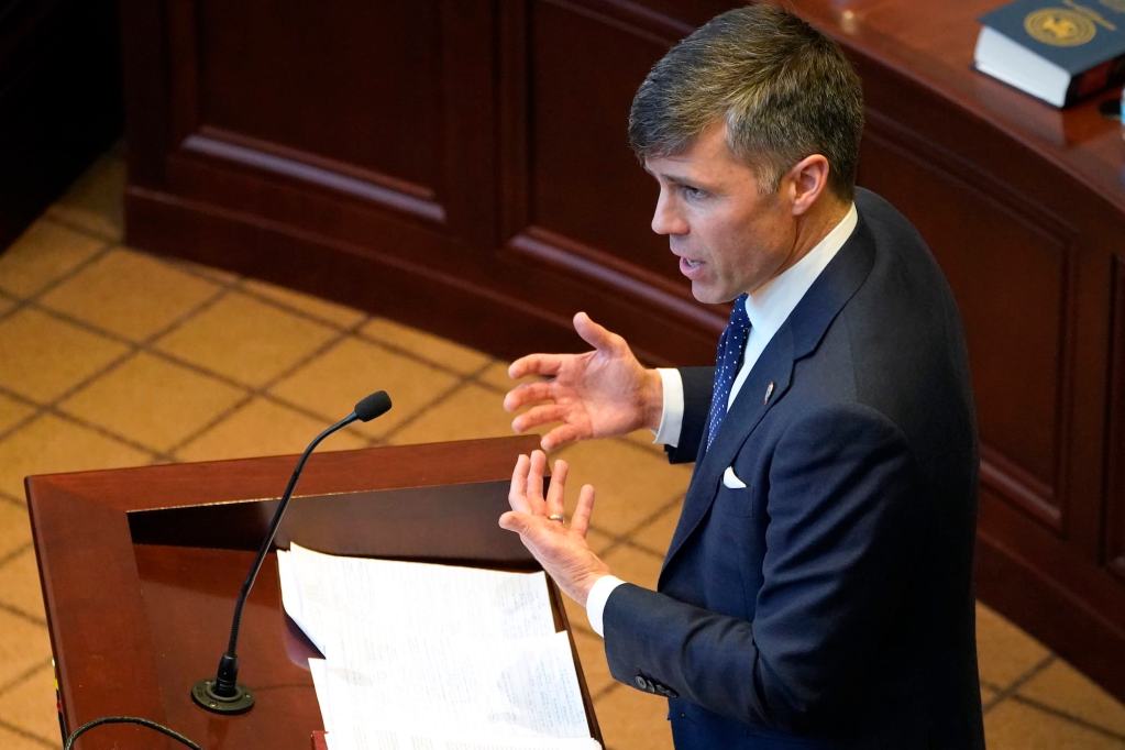 A view from above of a man in a suit at a podium, gesturing with his hands as he speaks