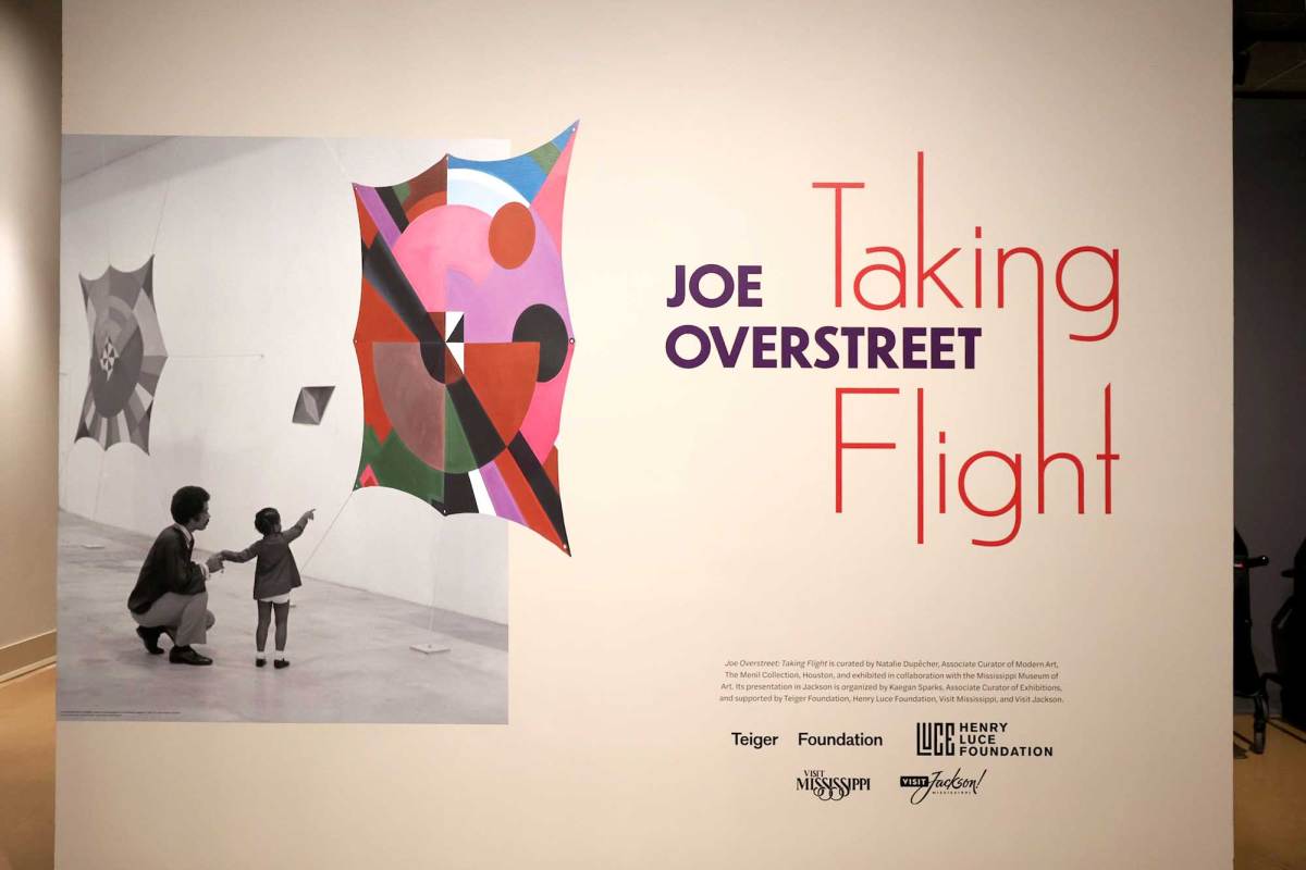 A sign that reads 'Joe Overstreet - Taking Flight'. An image of a Man and little girl pointing at colorful artwork is seen on the left hand side