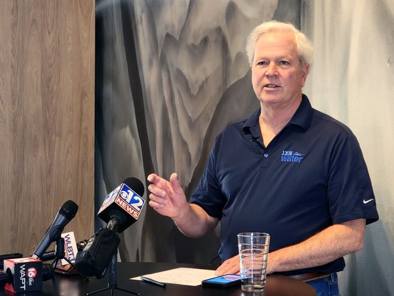 JXN Water head Ted Henifin speaks at a press conference before local news station mics.