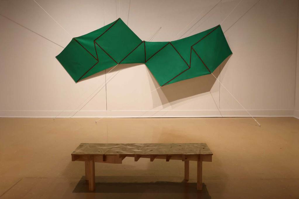 A simple bench sits in front of a large green geometric piece of artwork hanging on the opposite wall