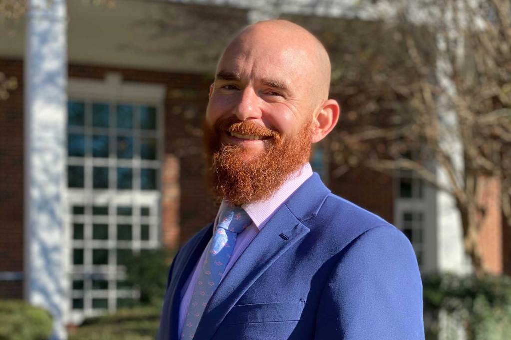 A bearded man in a suit poses for a portrait outside