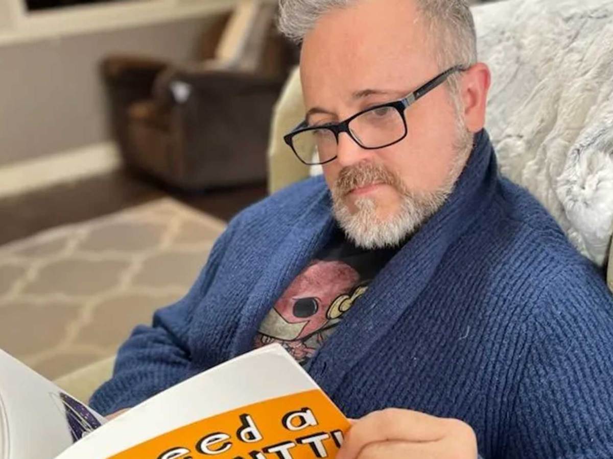 A man sits in a living room chair and reads the book 'I Need A New Butt'