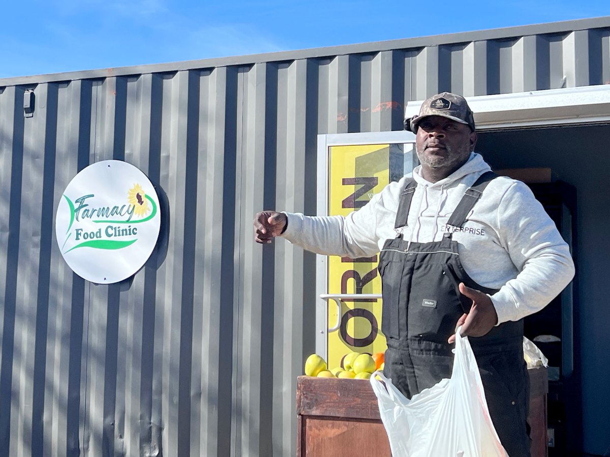 A black man holds a grocery bag in front of a store