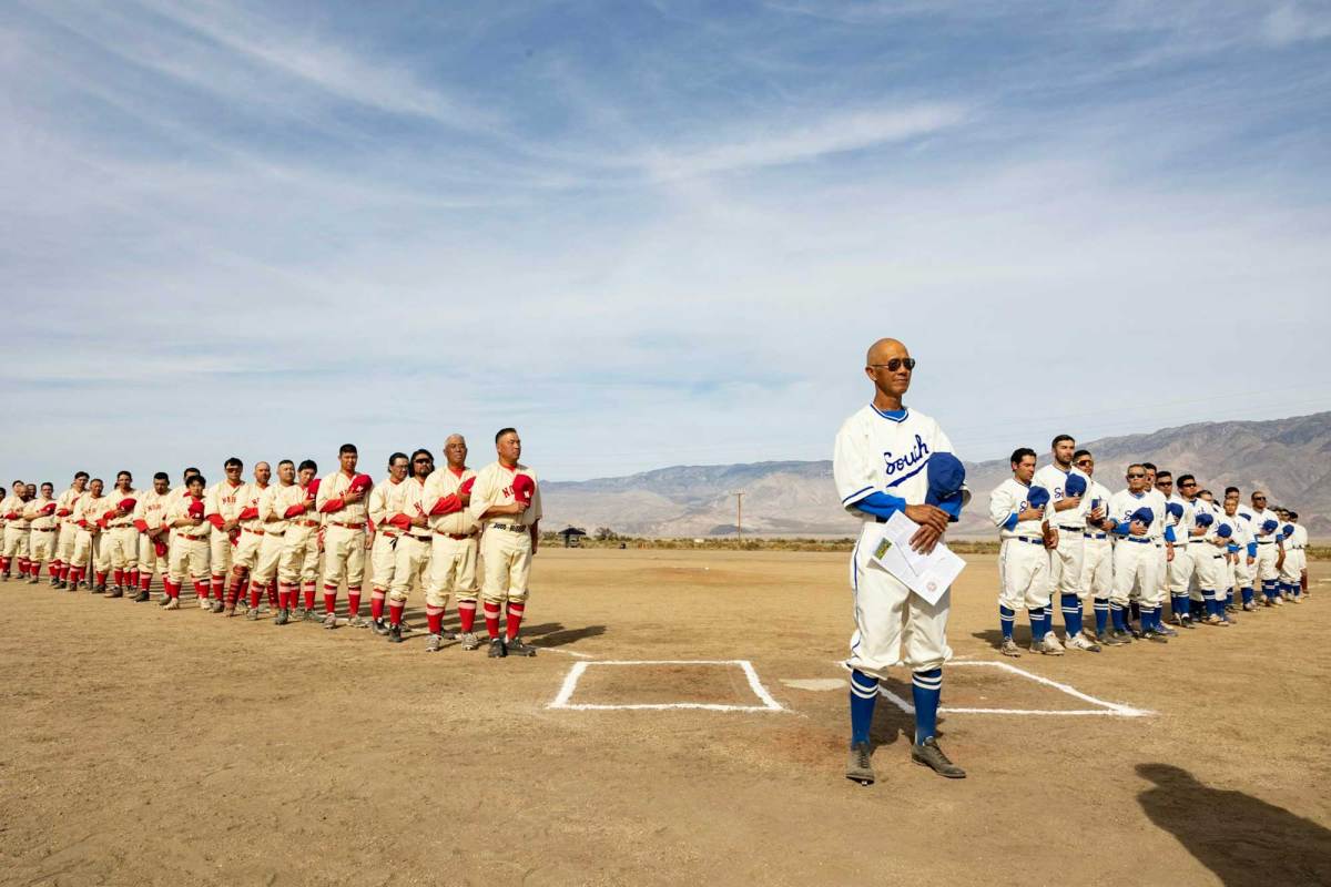 Two teams of baseball players in separate lines. One team is wearing white uniforms with blue trim, the other wearing light-tan uniforms with red trim.