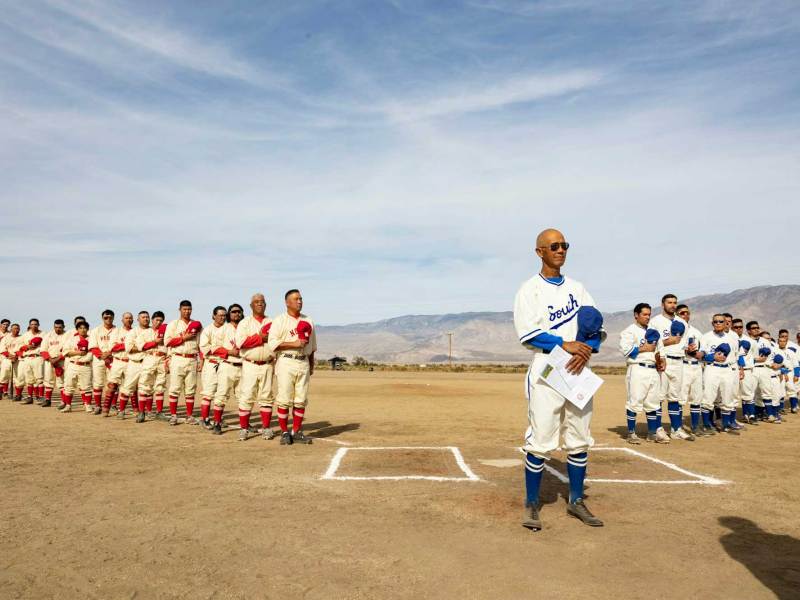 Two teams of baseball players in separate lines. One team is wearing white uniforms with blue trim, the other wearing light-tan uniforms with red trim.