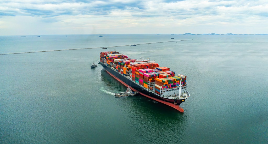 A shipping vessel carrying numerous shipping containers at sea.