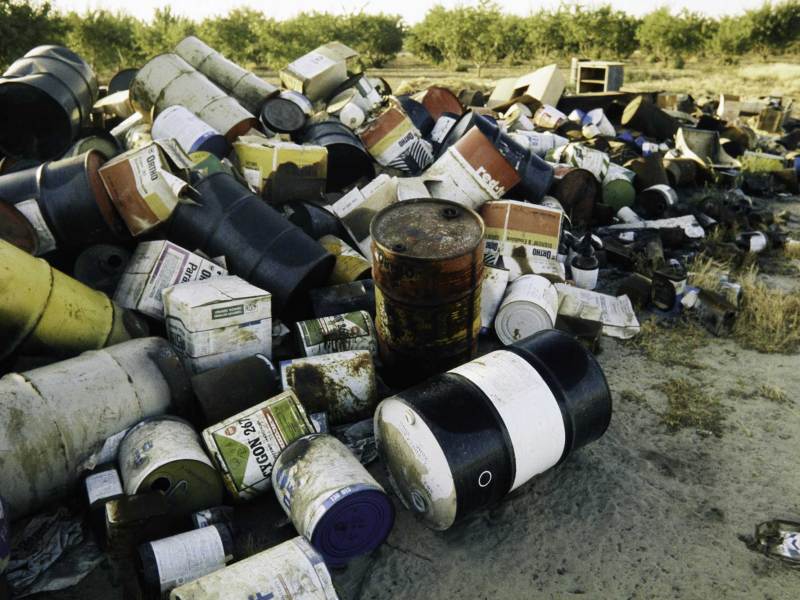 Several dirty barrels, boxes and other refuse in a pile.