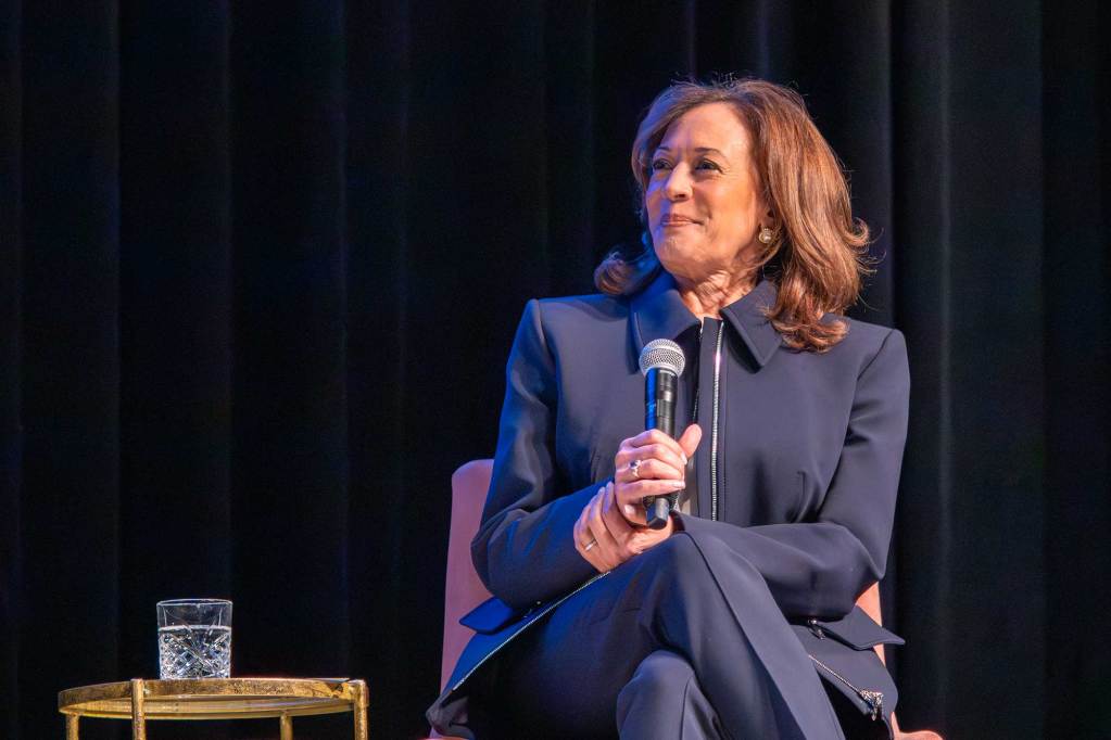 Kamala Harris, seated on stage, listening to someone speak
