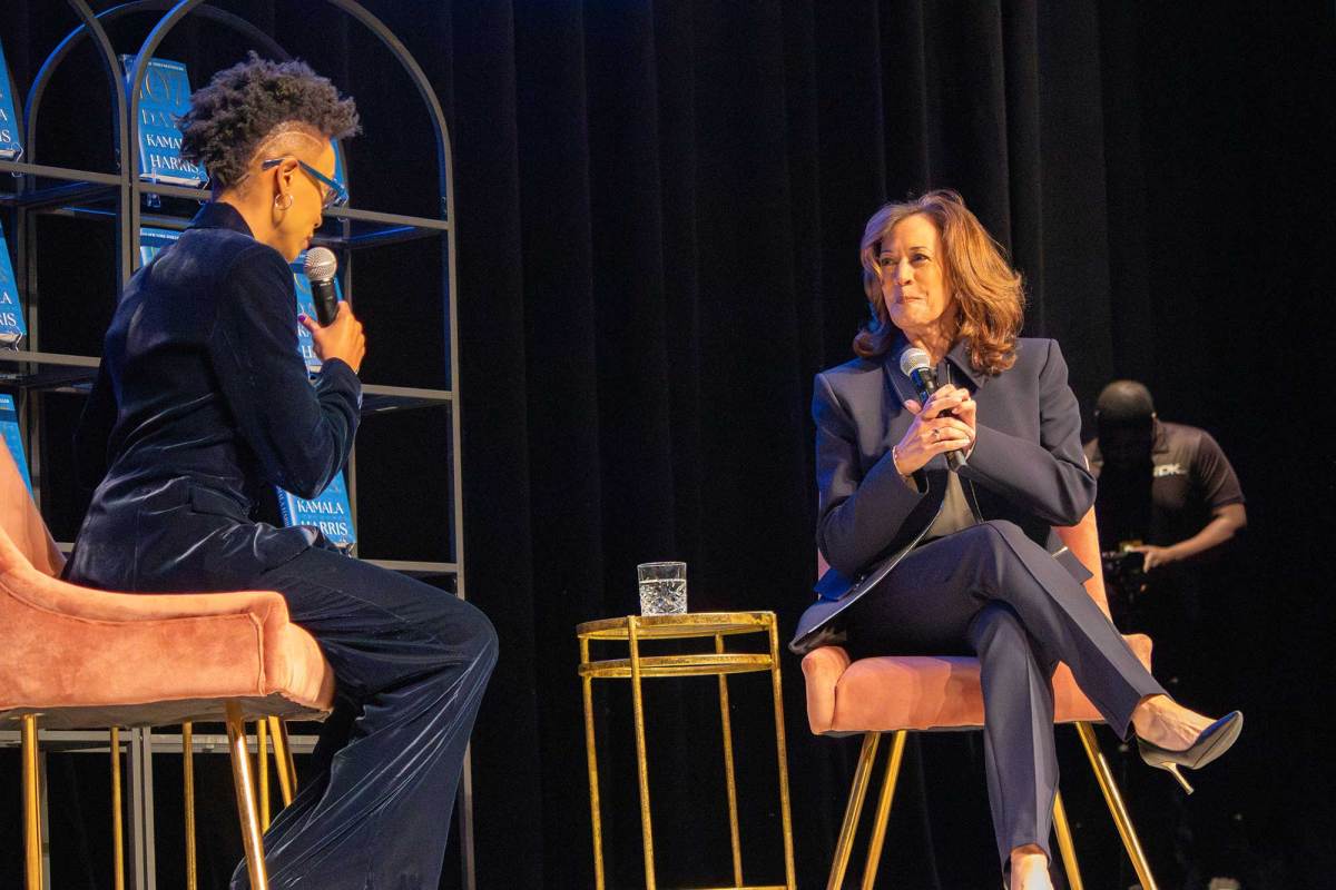 Rita Brent and Kamala Harris speak on stage, seated in pink chairs and backed by shelves holding Harris's new book 107 Days