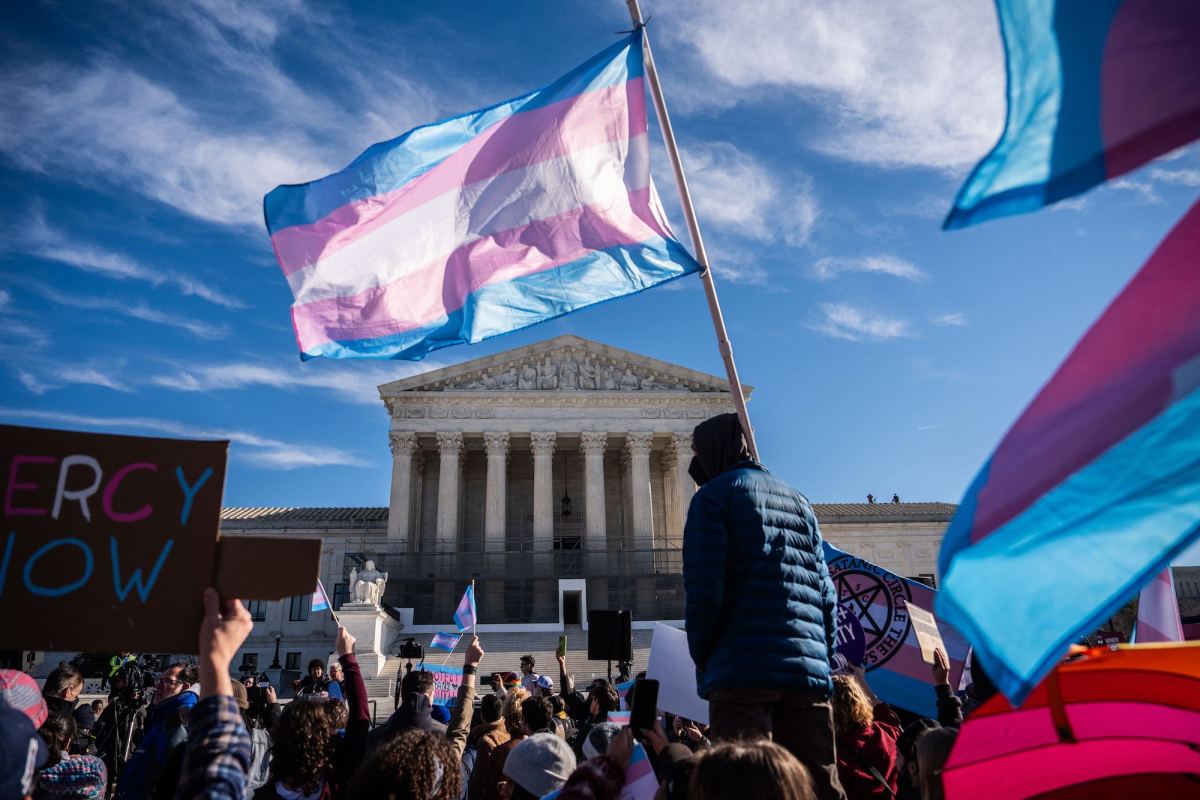 A transgender pride flag flies among a large crowd of demonstrators in front of the U.S. Supreme Court building.