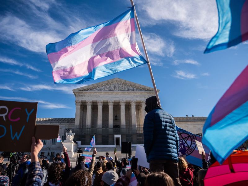 A transgender pride flag flies among a large crowd of demonstrators in front of the U.S. Supreme Court building.