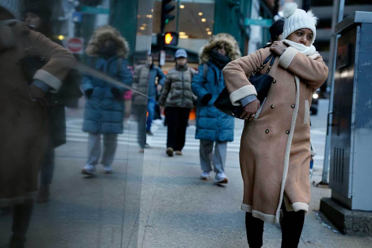 A woman wearing a winter coat, white winter hat and carrying a purse walking with several other people dressed in winter clothing in the background.