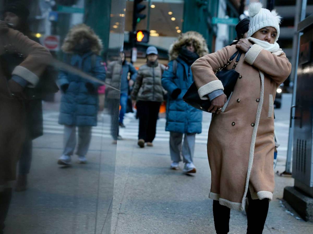 A woman wearing a winter coat, white winter hat and carrying a purse walking with several other people dressed in winter clothing in the background.