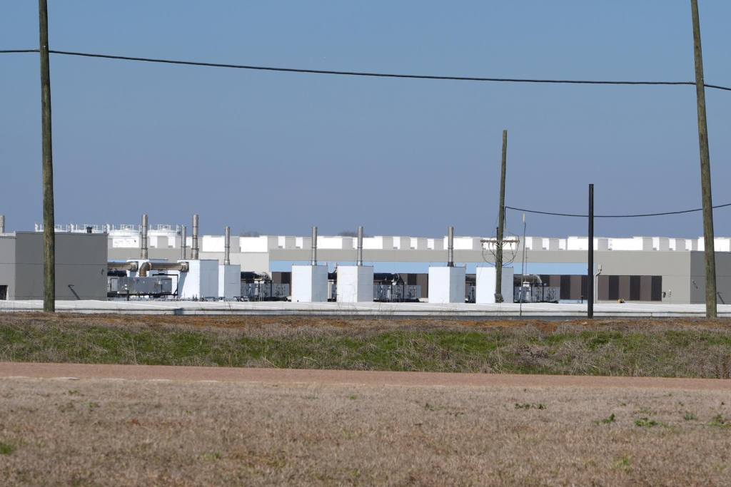 A view of a white and grey data center seen across a green field