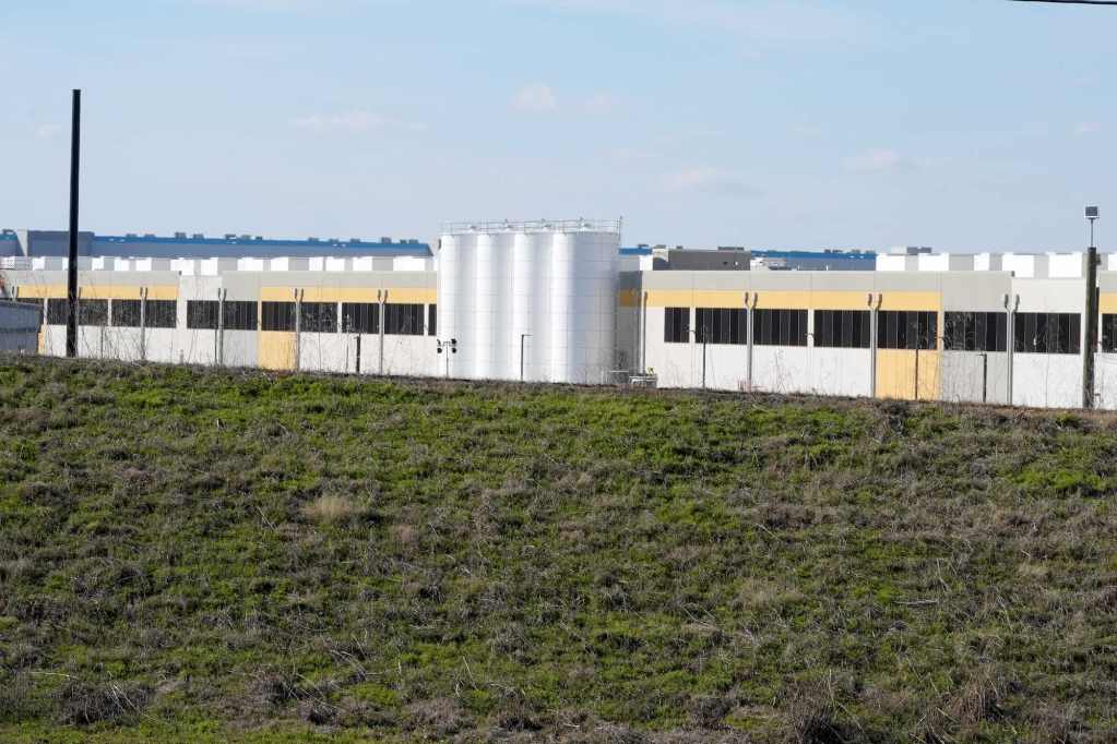 A grey, white and yellow data center sits beyond a green field