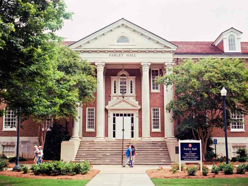 People walk past a campus building labeled Farley Hall
