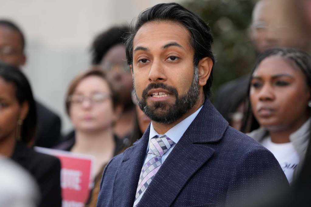 Amir Badat seen speaking at a press conference outside, with people seen behind him