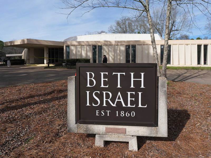 A sign that reads 'Beth Israel Est 1860' in front of the synagogue. A security person is walking by and the front door is wrapped in yellow caution tape