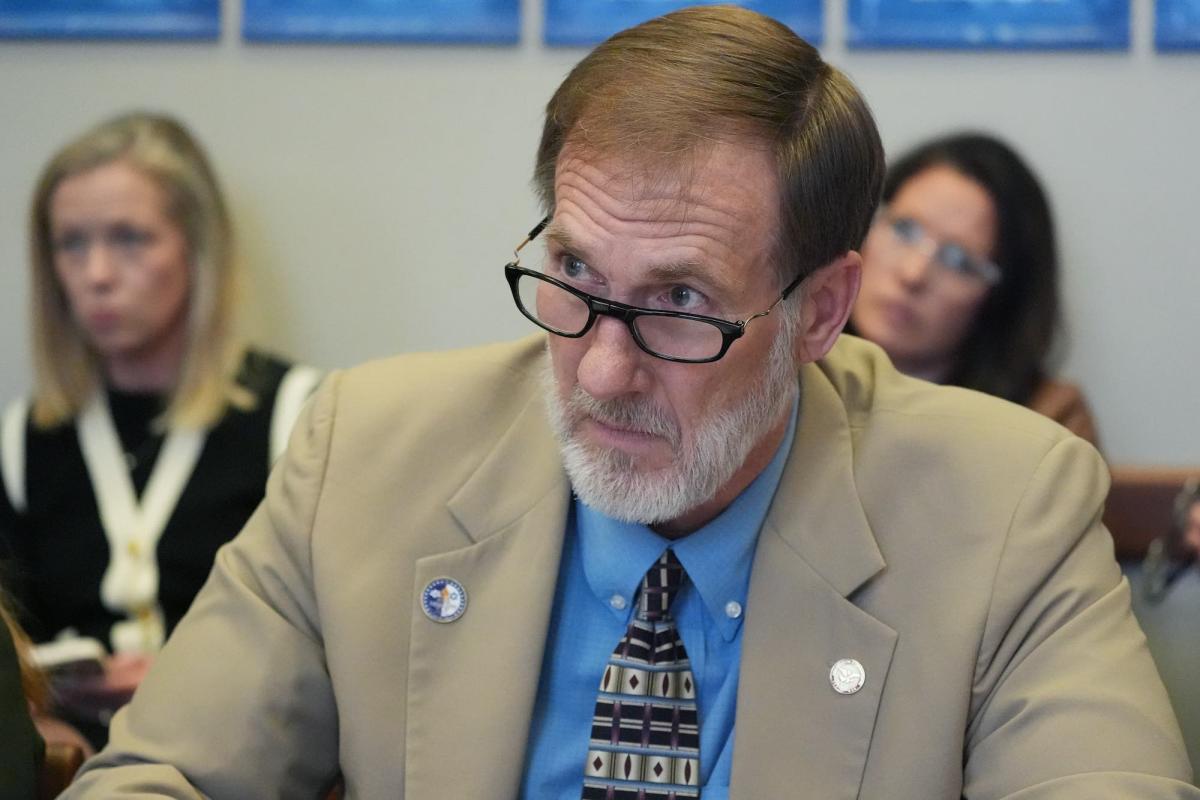 A closeup of Charles Blackwell, wearing glasses and a tan suit, sitting in a committee meeting