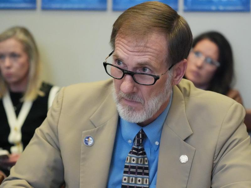 A closeup of Charles Blackwell, wearing glasses and a tan suit, sitting in a committee meeting