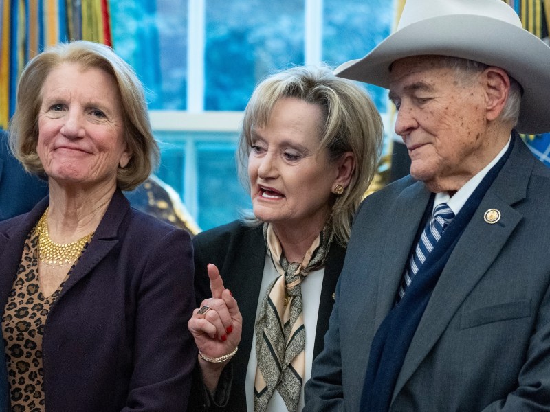 a photo of a woman holding a finger up and speaking in the center surrounded by another woman who is smiling and a man in a cowoby hat