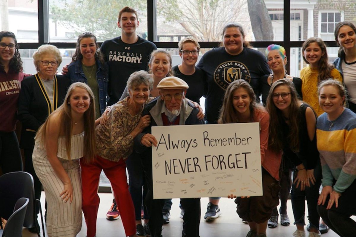 Two rows of people posing for a picture, with people in the first row holding a sign that says, “Always Remember, Never Forget.”