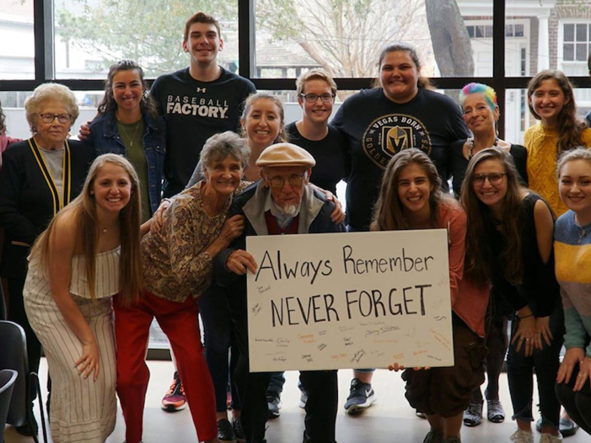 Two rows of people posing for a picture, with people in the first row holding a sign that says, “Always Remember, Never Forget.”
