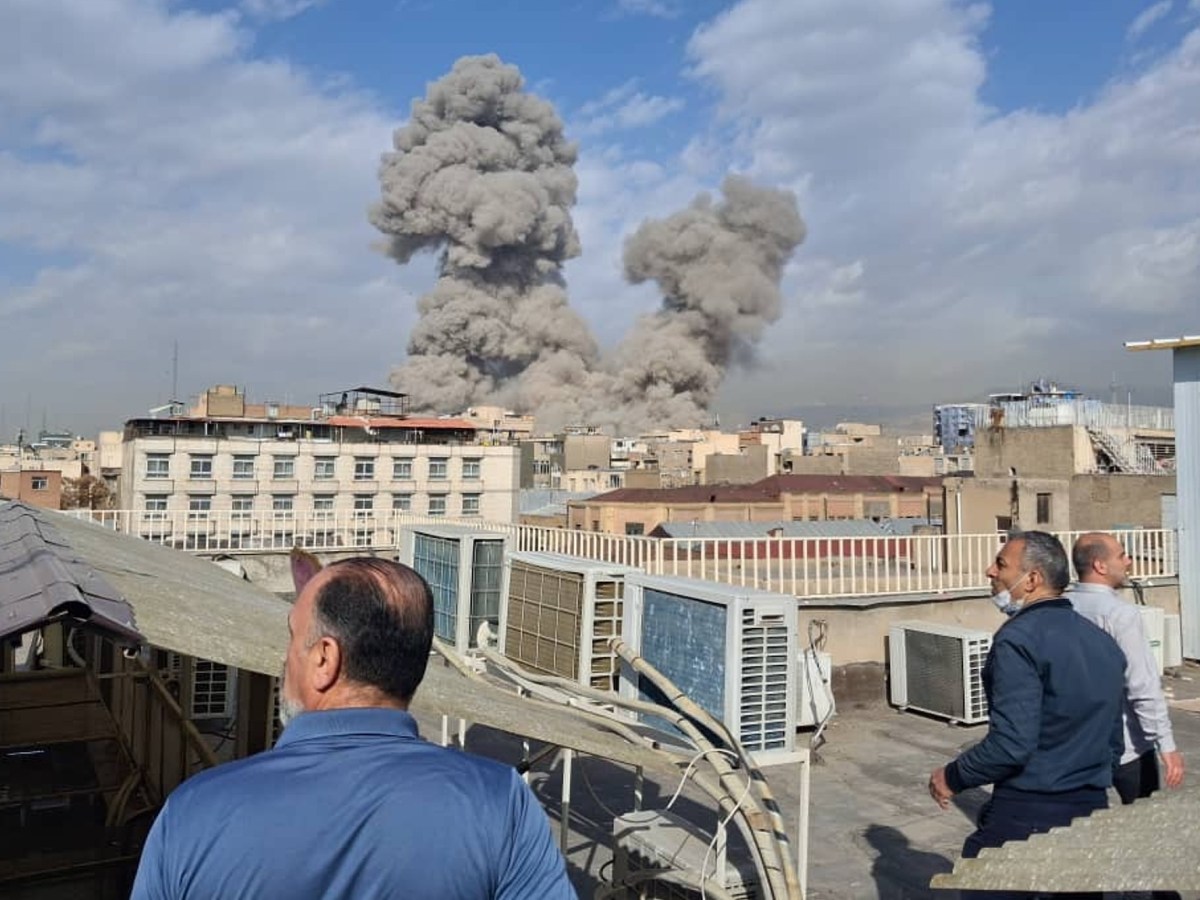 a photo shows men looking as smoke from explosions rrises from behind a row of buildings