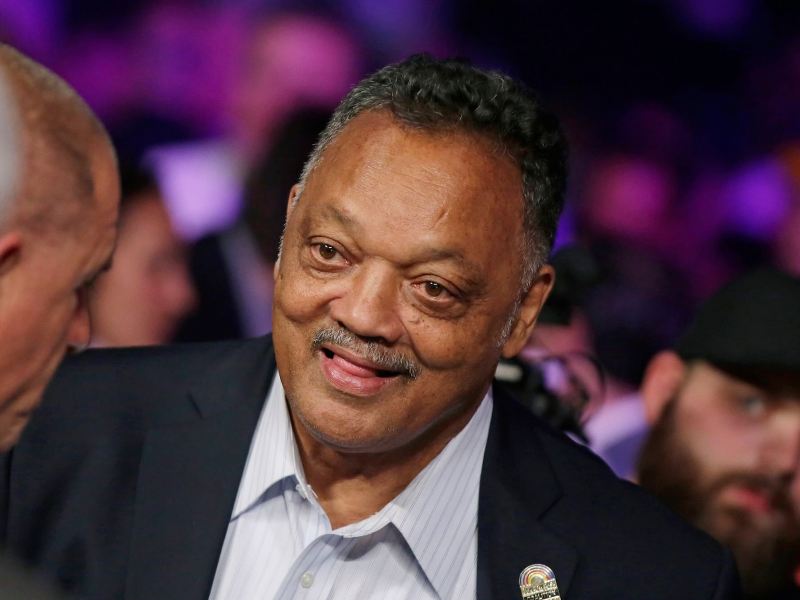 Jesse Jackson standing to greet someone in a crowd
