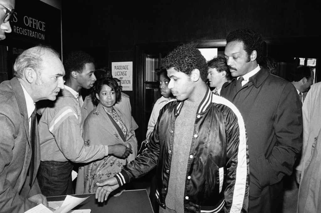 An old black and white photo with Jesse Jackson standing behind a young man registering to vote