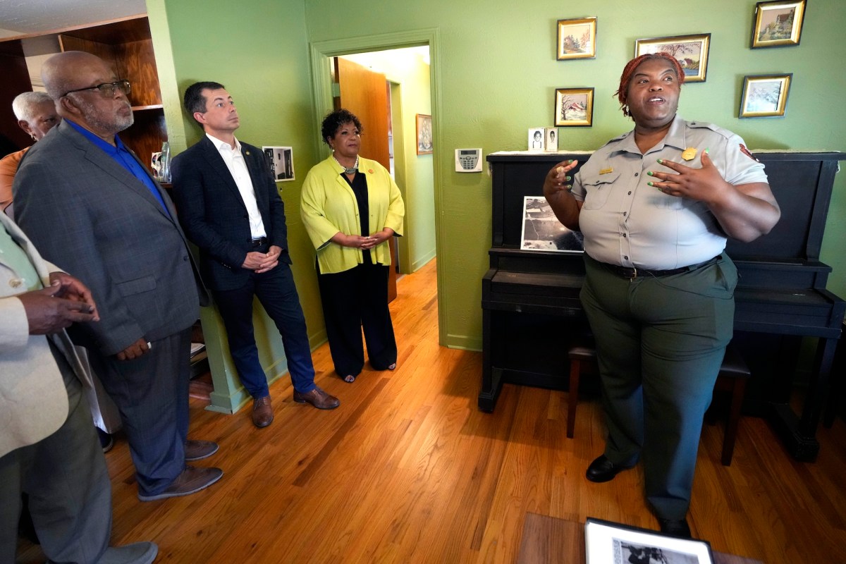 a woman in a National Park Service Uniform talking in a room with green walls and a piano while two men and a woman listen