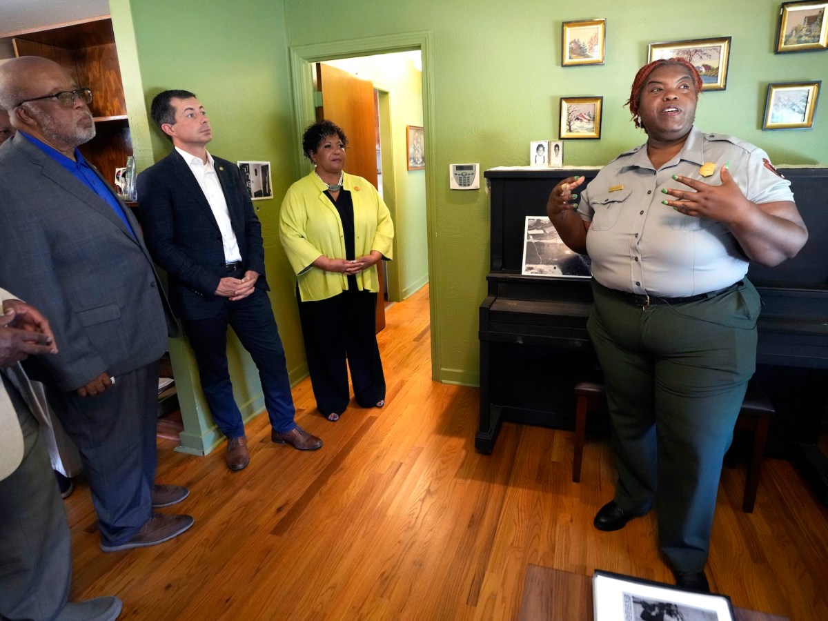 a woman in a National Park Service Uniform talking in a room with green walls and a piano while two men and a woman listen