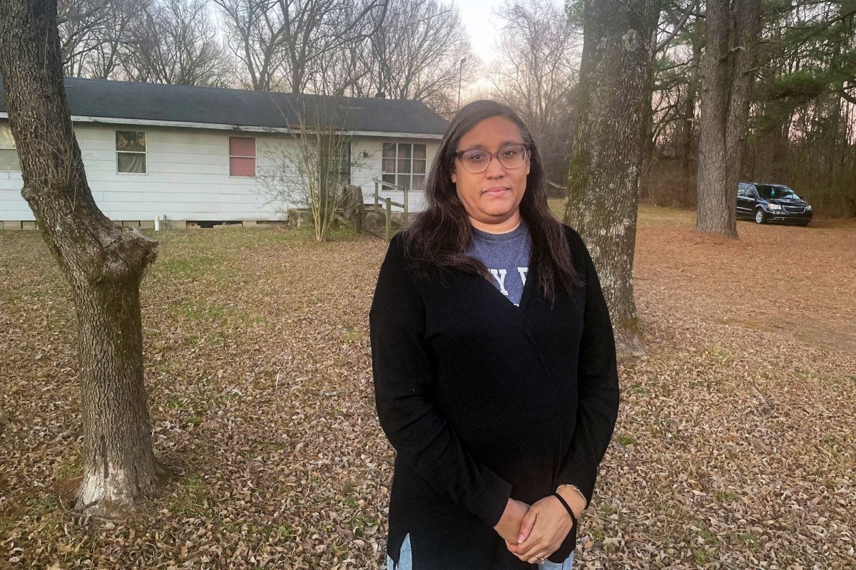 A woman wearing glasses stands in the yard of her house