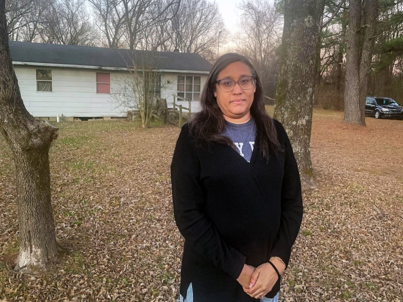 A woman wearing glasses stands in the yard of her house