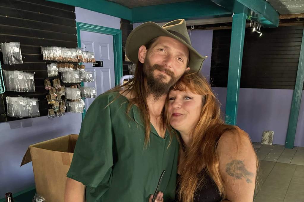 Two people pose together inside a green and purple storefront