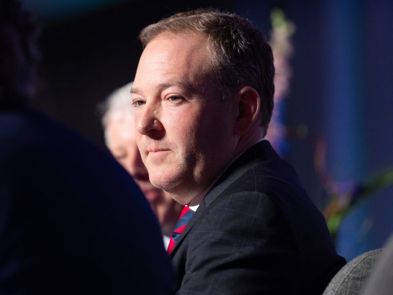 A man wearing a suit facing the camera looking to the person to his left.