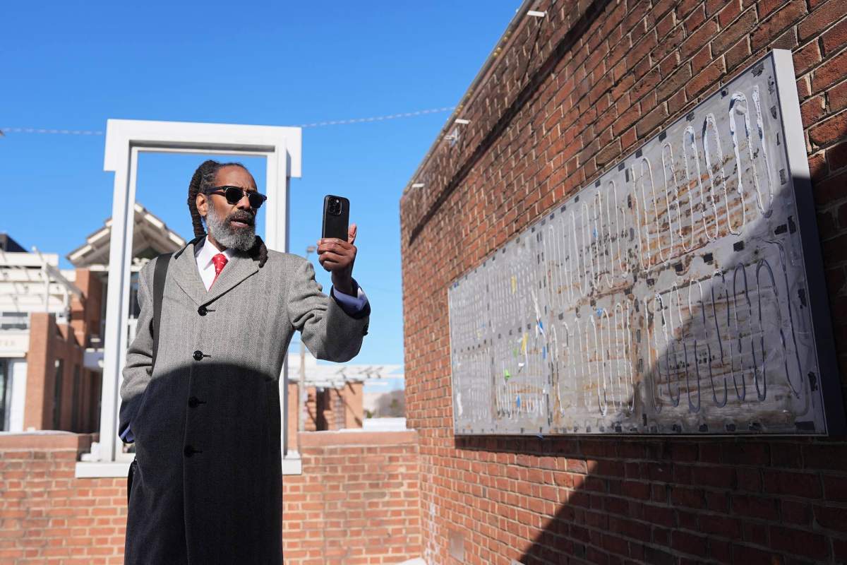 A man stands outside of a brick structure and documents changes in the space with his phone