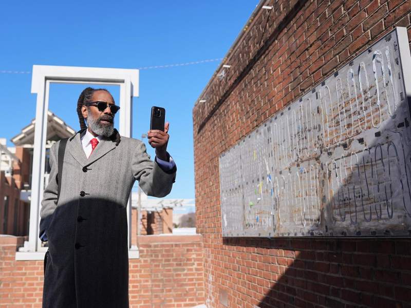 A man stands outside of a brick structure and documents changes in the space with his phone