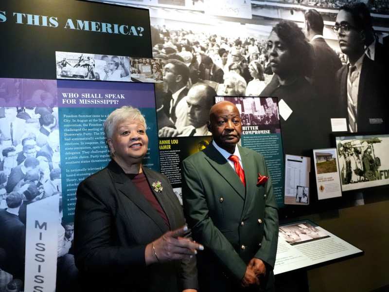 A woman and man, both wearing suit jackets, standing in front of a display with several black-and-white photos and descriptive text.