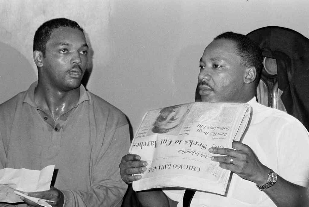 An old black and white photo of Jesse Jackson with Martin Luther King Jr. looking at a newspaper together