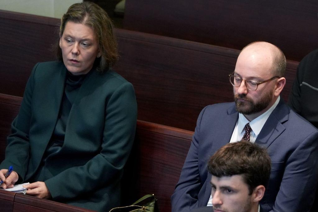 Two people sit in benches in a court listening to lawyers