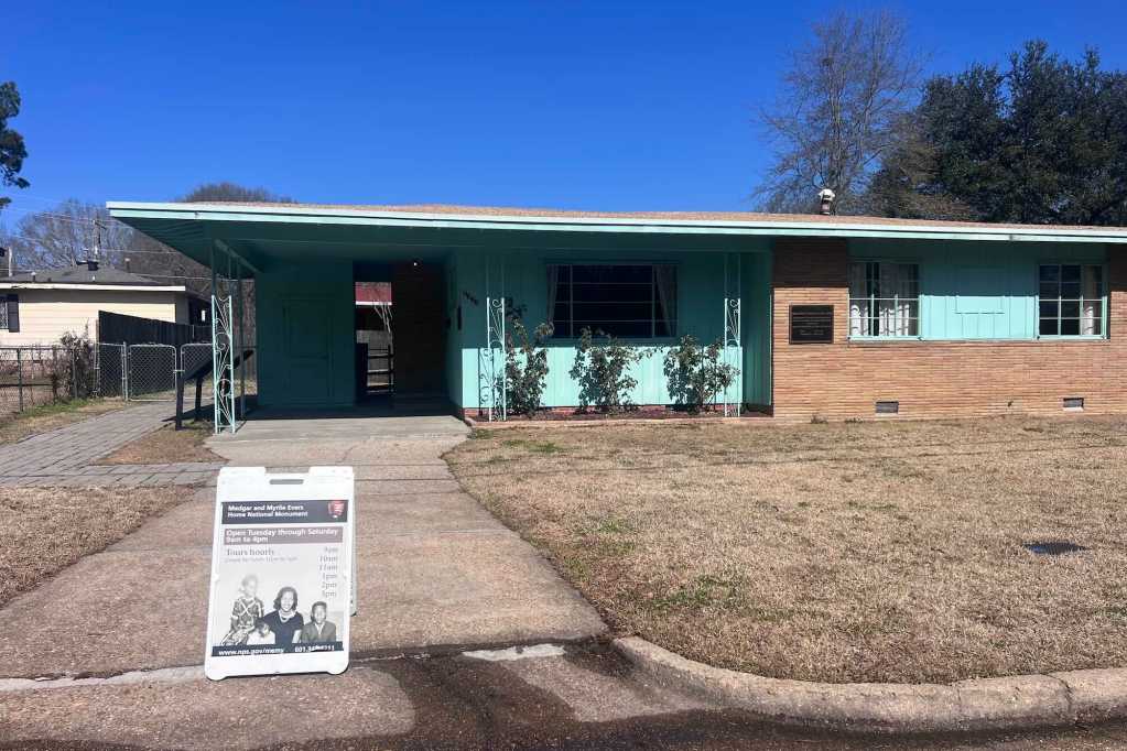 a mint green and brick mid-century home has a sign in the driveway with hours on it