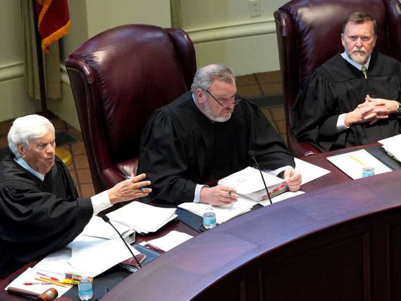 Three justices listening and speaking from their seats behind the bench