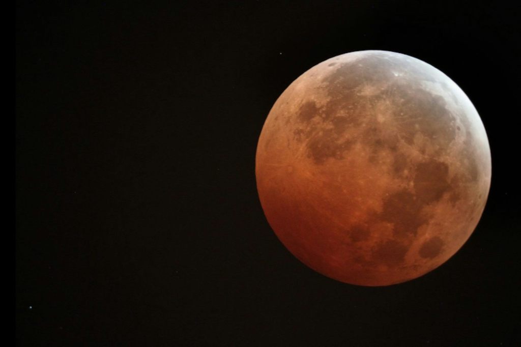 A photo of the Moon with a reddish hue against a pitch-black sky.