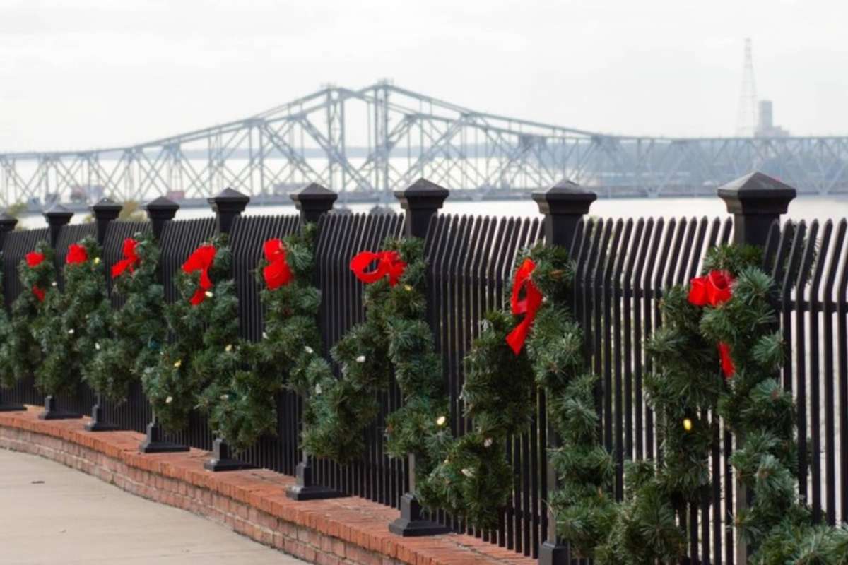 A fence decorated with several wreaths, with a bridge in the background.