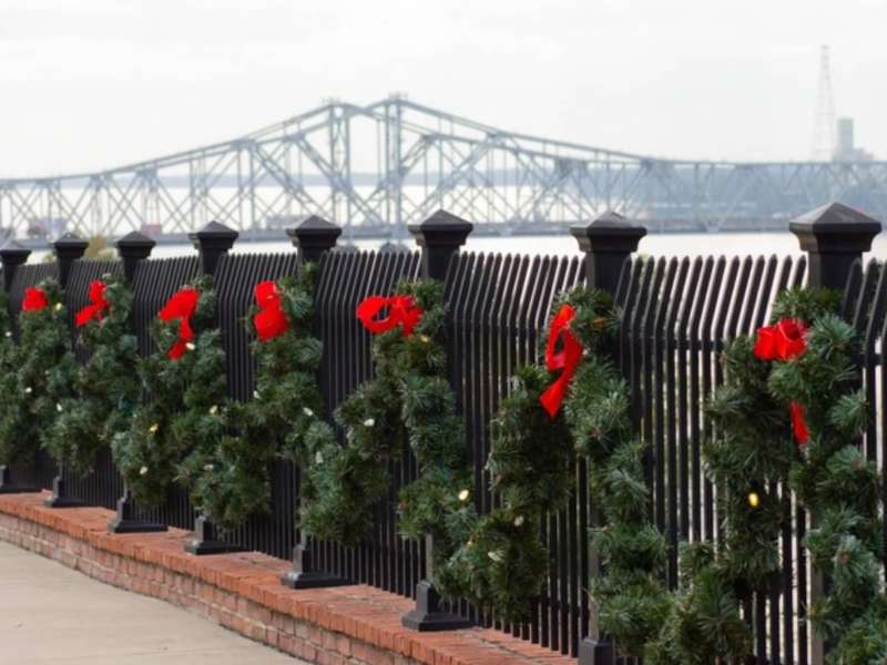 A fence decorated with several wreaths, with a bridge in the background.