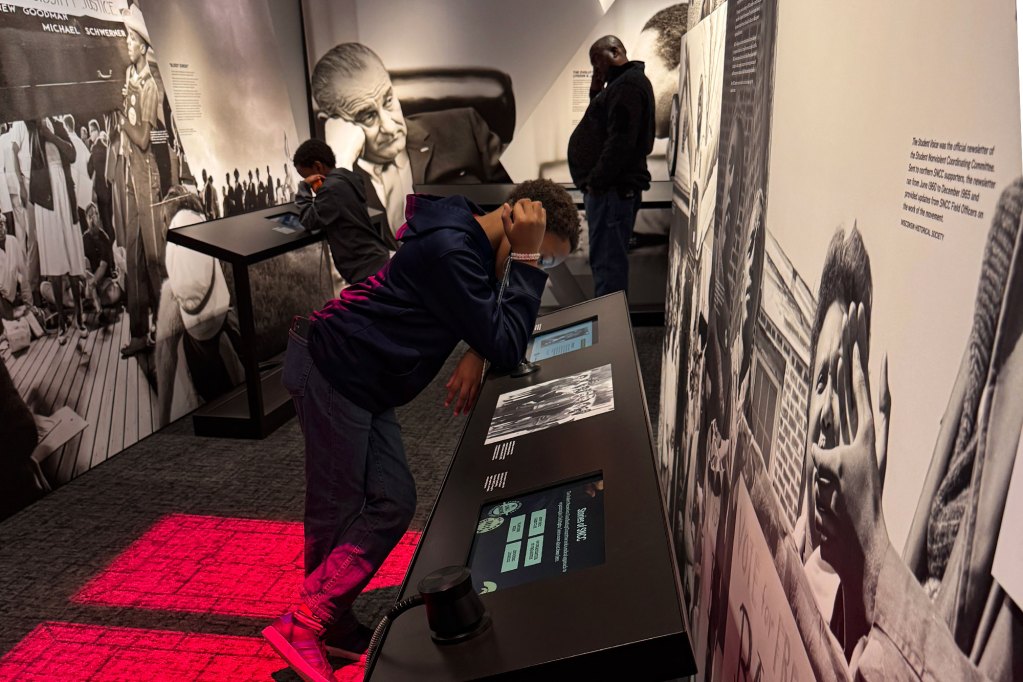 Two boys lean at opposite displays and reads the digital displays in a civil rights museum